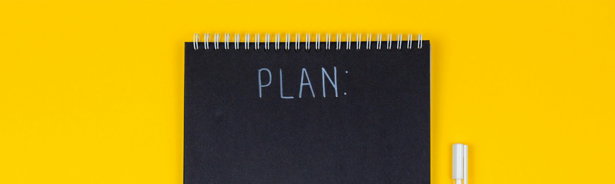 Black notebook with the word 'Plan' behind the yellow desk.